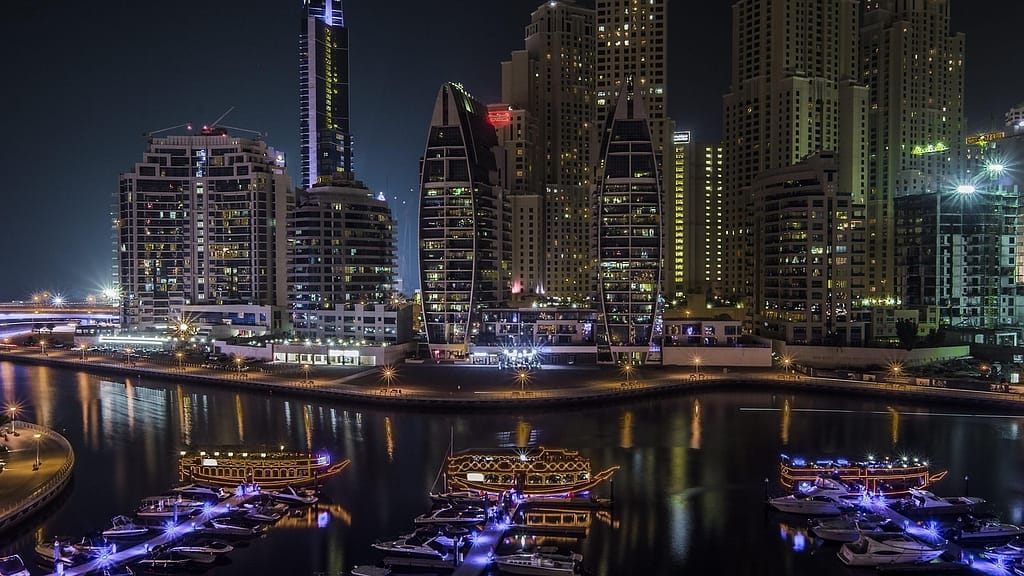 Nachtelijk uitzicht op Dubai met moderne, verlichte wolkenkrabbers en boten met sfeerverlichting in de haven.