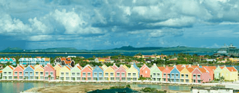 Kleurrijk Bonaire met pastelkleurige huizen onder een dramatische, bewolkte hemel. Kalm water en heuvels in de verte creëren een serene sfeer.