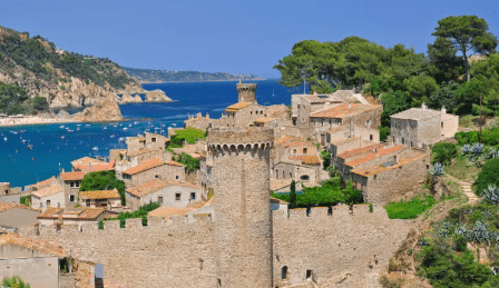 Uitzicht op het historische centrum en de middeleeuwse stadsmuren van Tossa de Mar aan de Costa Brava, met blauwe zee en groene heuvels op de achtergrond.